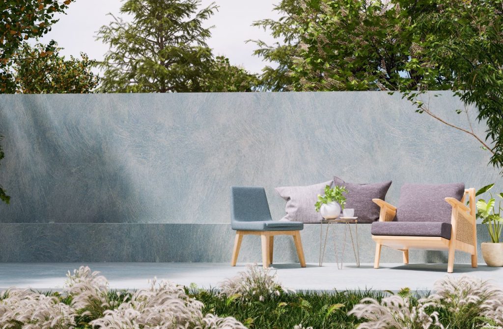 Modern garden with a concrete wall around it, will chairs and soft purple and blue cushions. 